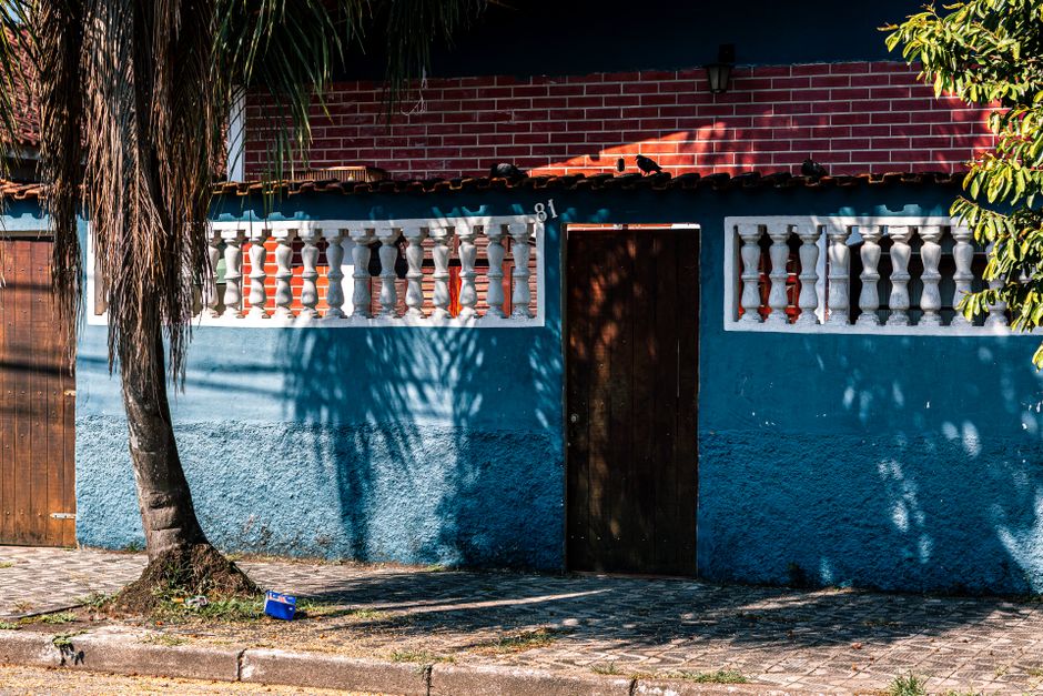 A vibrant blue and red house facade with shadowed palm in sunny outdoor setting.