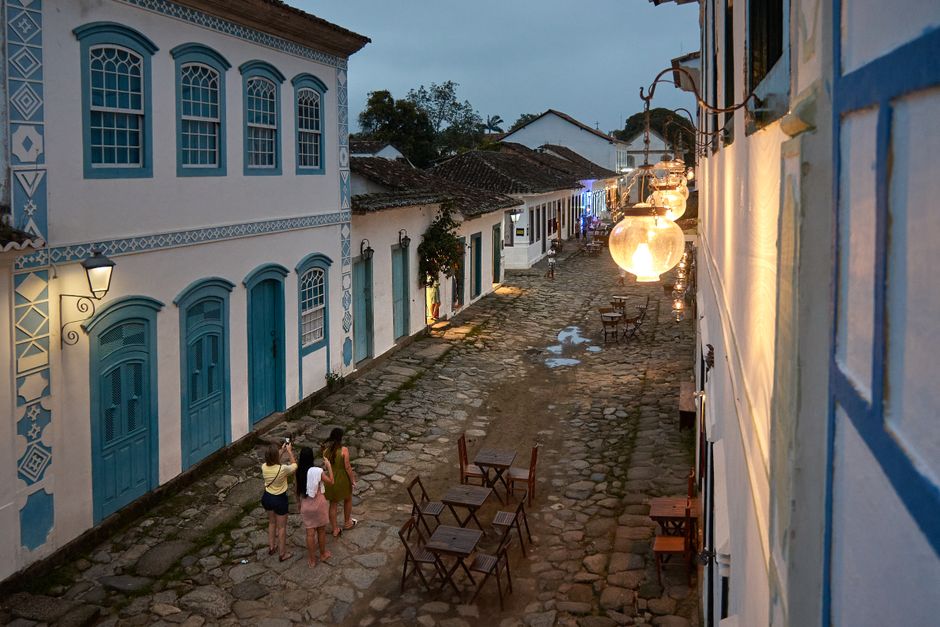 Three women strolling down a cobblestone street in Paraty, Brazil, illuminated by warm streetlights.