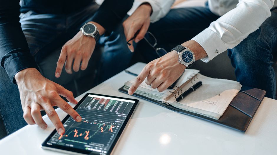 Two businessmen discussing financial data on a tablet during a meeting.
