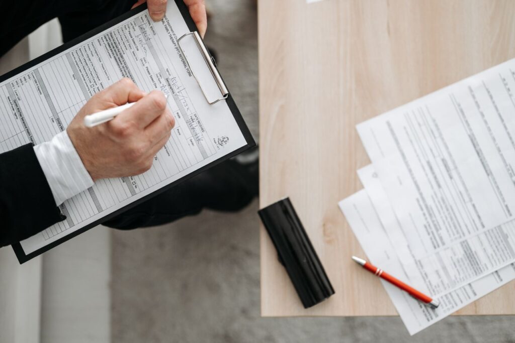 High-angle view of a person filling out forms on a clipboard, emphasizing paperwork and documentation.